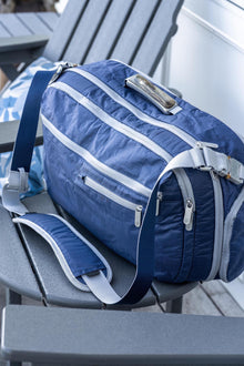 Offsite Work-to-Water Bag in Ocean blue Dyneema resting on an outdoor chair, featuring a wood-inlay aluminum handle and adjustable messenger strap
