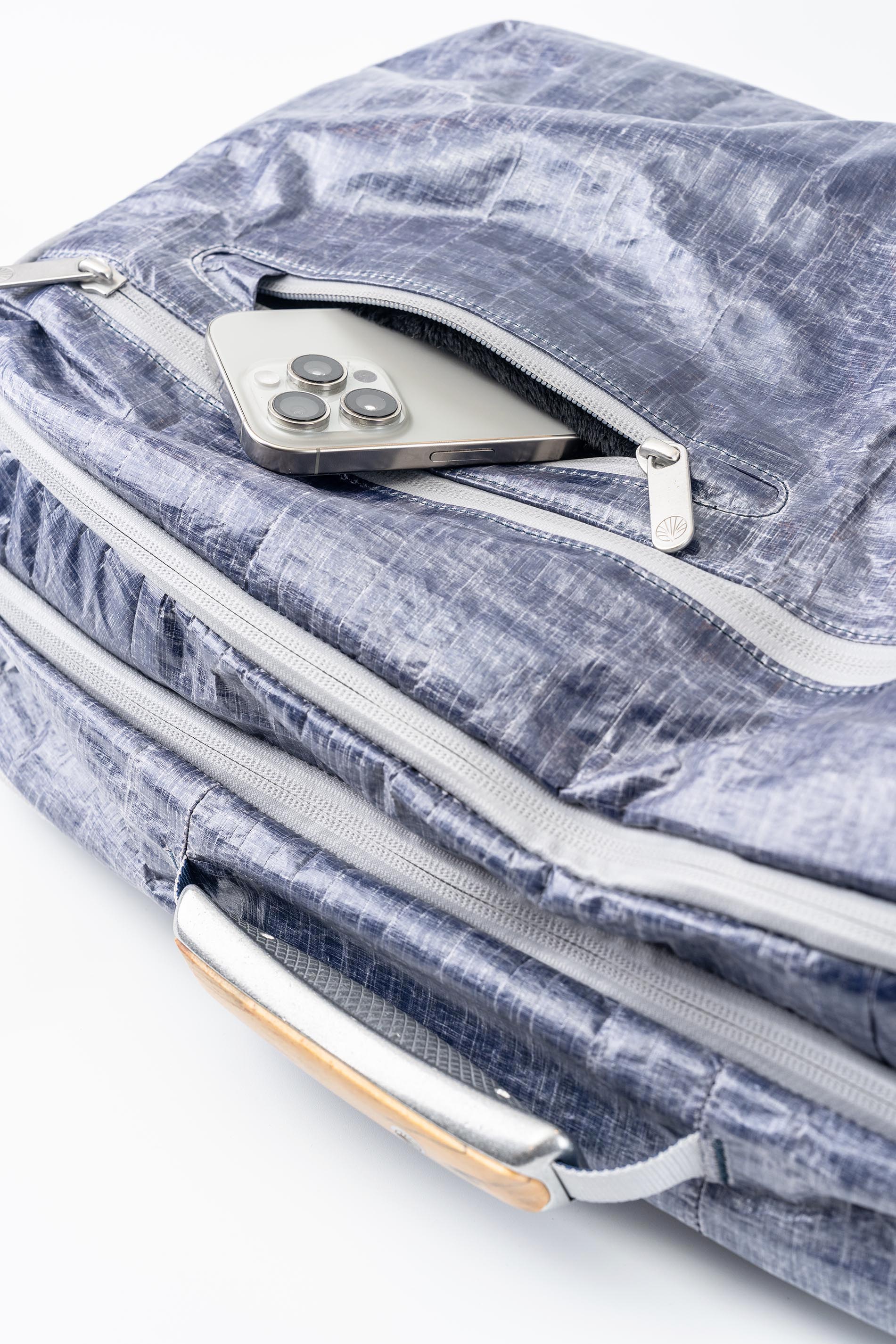 Blue textured bag with a silver zipper, phone sticking out of pocket, and handle, white background