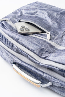 Blue textured bag with a silver zipper, phone sticking out of pocket, and handle, white background