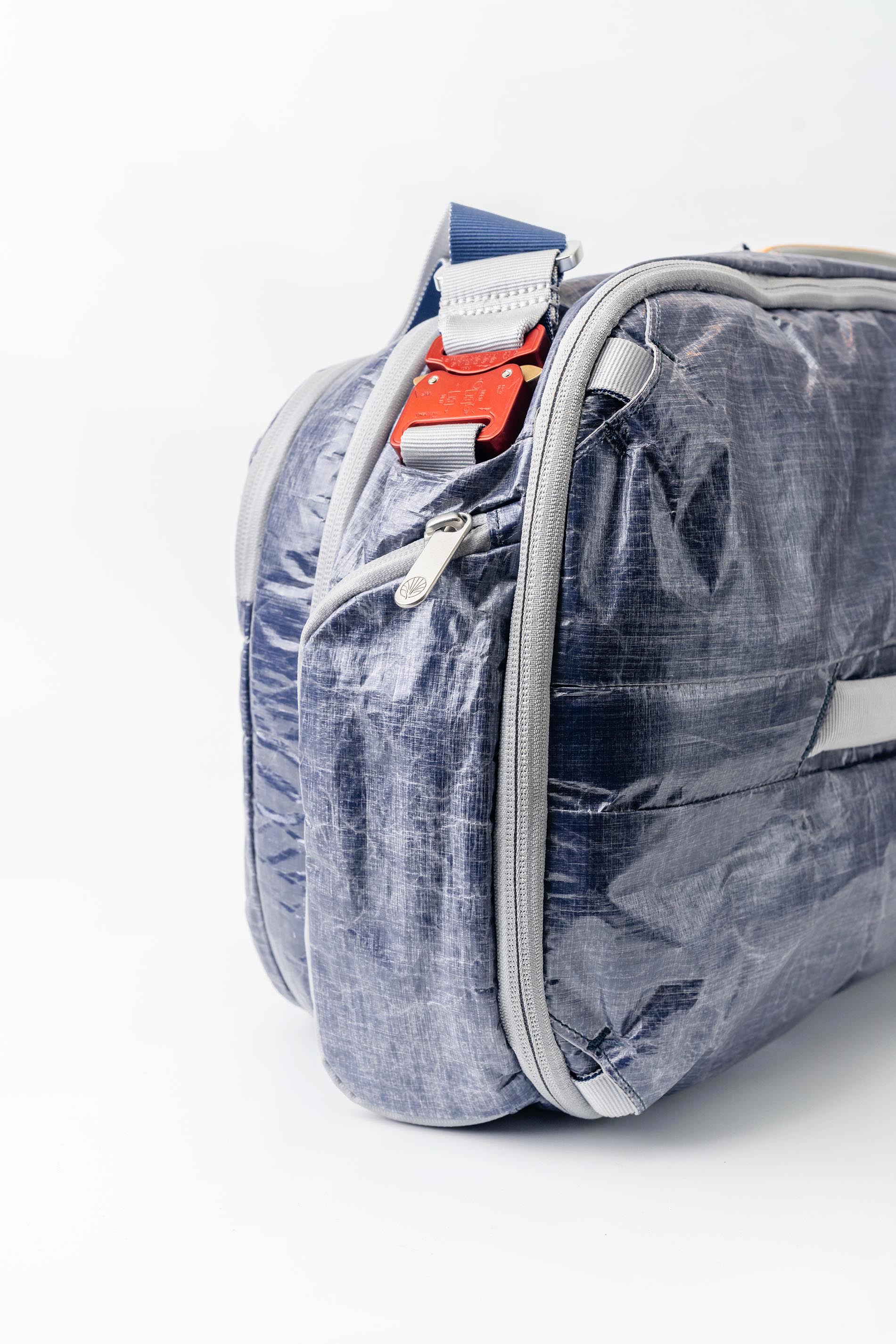 Side view of "White Cap" Work to Water Blue and gray bag with a red tag on a white background