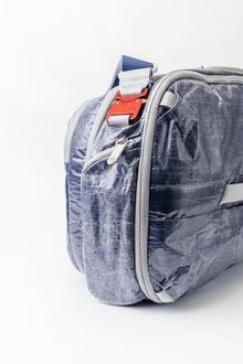 Side view of "White Cap" Work to Water Blue and gray bag with a red tag on a white background