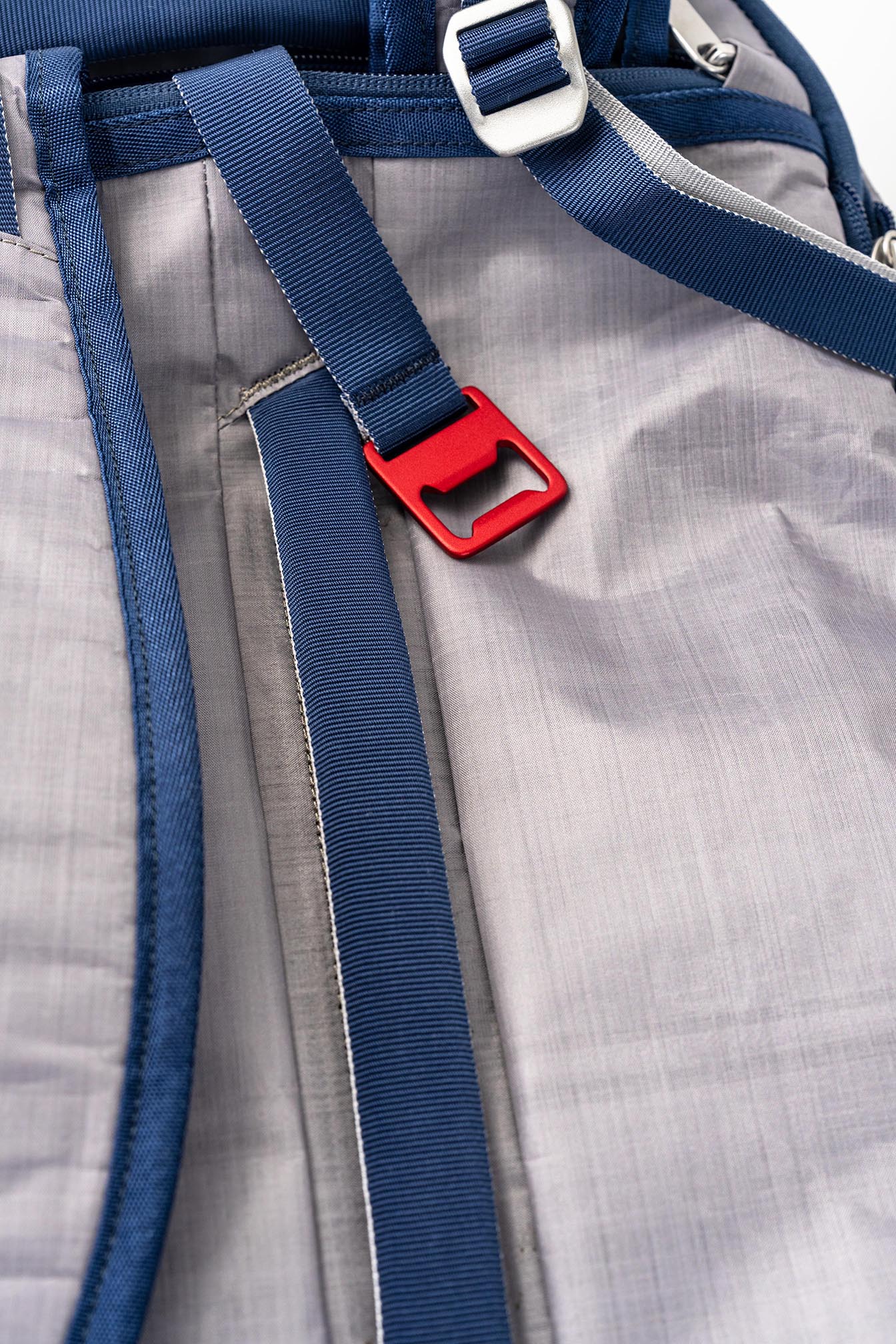 Close-up of the Offsite Haze Gray Work-to-Water bag showing blue webbing straps and a red anodized aluminum bottle opener on Dyneema fabric.
