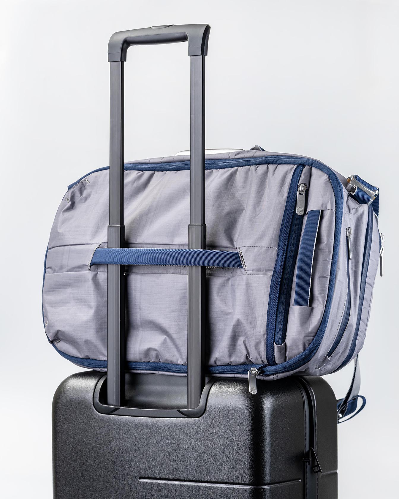 Rear view of the Offsite Work-to-Water Bag in Haze gray Dyneema, shown secured to a rolling suitcase using the built-in luggage pass-through