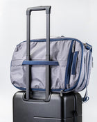 Rear view of the Offsite Work-to-Water Bag in Haze gray Dyneema, shown secured to a rolling suitcase using the built-in luggage pass-through