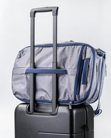 Rear view of the Offsite Work-to-Water Bag in Haze gray Dyneema, shown secured to a rolling suitcase using the built-in luggage pass-through