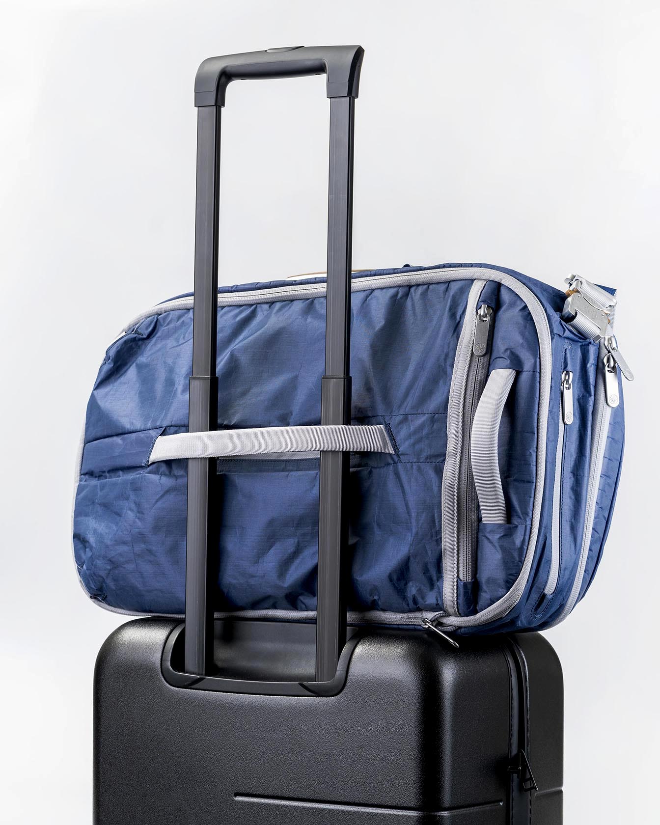 Rear view of the Offsite Work-to-Water Bag in Ocean blue Dyneema, shown secured to a rolling suitcase using the built-in luggage pass-through
