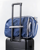 Rear view of the Offsite Work-to-Water Bag in Ocean blue Dyneema, shown secured to a rolling suitcase using the built-in luggage pass-through