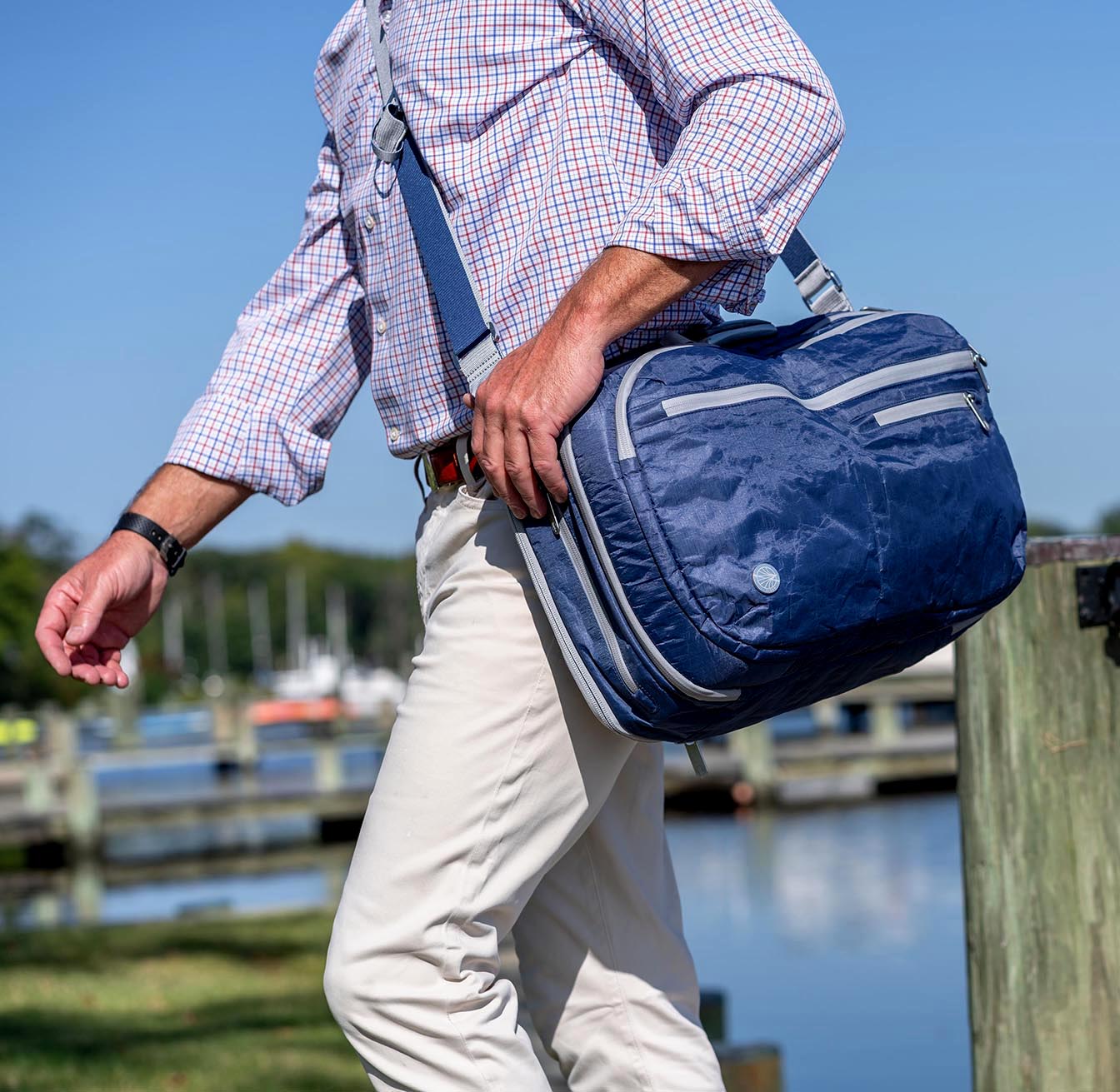 Person carrying the Offsite Work-to-Water Bag in Ocean blue by the waterfront, showing messenger carry and everyday travel use